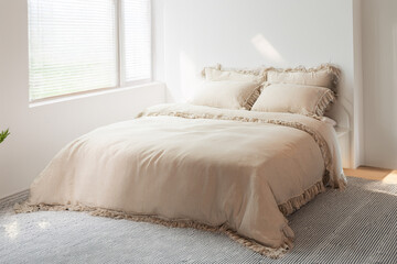 Minimalist cozy bedroom with a double bed. Double empty bed with beige pillows with texture for the...