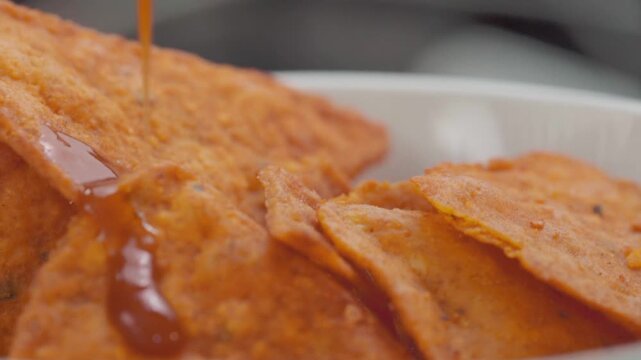 Pouring hot sauce on a bowl of crispy seasoned crackers; close-up