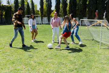Naklejka premium group of young latin american friends playing football in public park in Mexico, team of hispanic people in outdoor activities