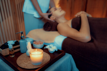 Aromatherapy massage ambiance or spa salon composition setup with focus decor candles and spa accessories on blurred woman enjoying blissful aroma spa massage in resort or hotel background. Quiescent