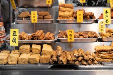 Vegetarian Chinese street food display of fried snacks and tofu at a market stall. English translation for Chinese words are vegetarian braised pork, spring rolls, tofu, and etc.