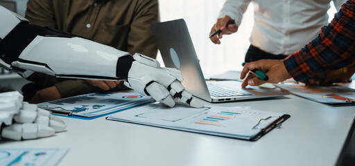 A modern office setting features a collaborative meeting where human hands and a robotic arm...