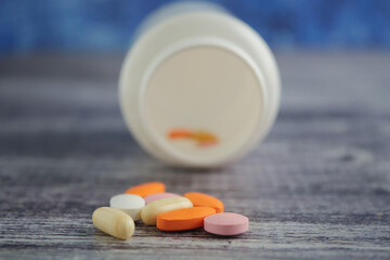 Colorful pills near a tipped bottle on wood