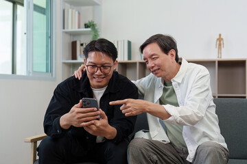 Digital Engagement. Two men enjoying a smartphone together while sitting on a couch.