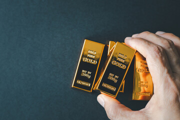 Close up of a hand holding a 999.9 fine gold bar from a stack on a dark background. Concept of...