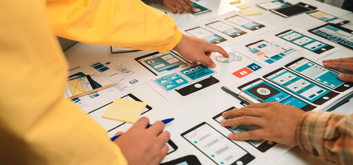 A vibrant workspace bustling with designers collaborating on a mobile app prototype, showcasing user interface wireframes, tools, and creative brainstorming approaches. SACTR