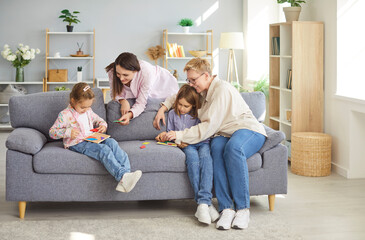 Happy family sitting on sofa inmodern living room, three generations of women are playing board...