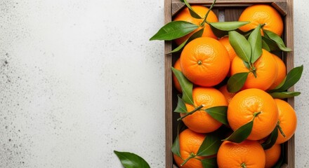 Fresh tangerines with green leaves in a wooden crate on a light textured surface, top view