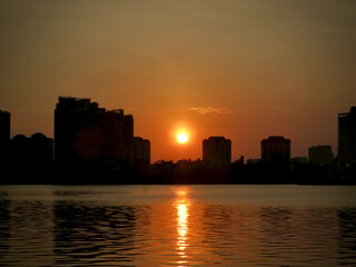 Warm Sunset Disk Above Urban Silhouettes with Shimmering Trail on West Lake in Hanoi, Vietnam