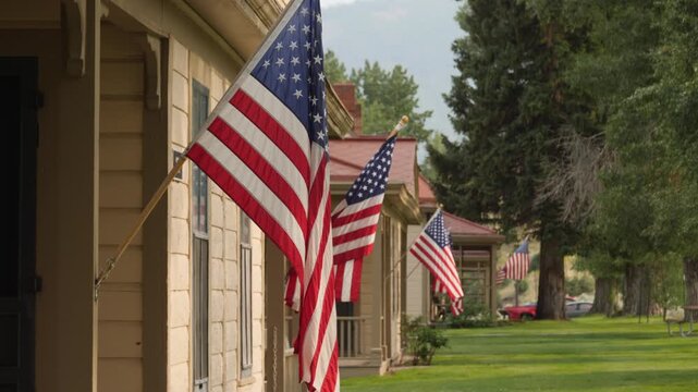 Historic homes adorned with rows of American flags on Memorial Day. Vibrant reds, whites, and blues contrast lush greenery in a nostalgic small-town USA scene. Bright daylight enhances charm.