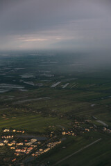 Obraz premium Vast flooded fields and villages seen from an aerial perspective under a cloudy sky, raining heavily over the upper area while the sun hits the lower part, creating a dramatic landscape in Thailand