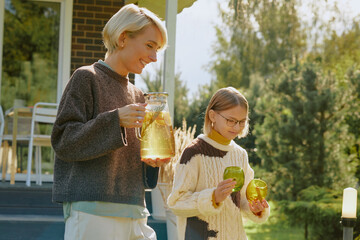 Caucasian woman carrying lemonade in glass pitcher with Caucasian girl holding two green glasses,...