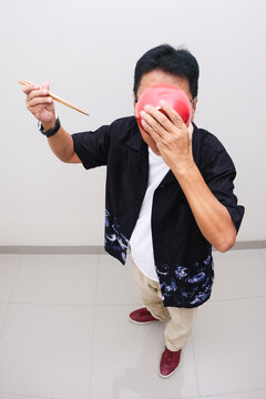 man sipping up soup from bowl covering his face