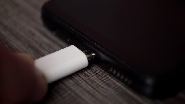 Hand Plugging USB-C Cable into Black Smartphone Charging Port Close Up