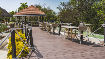 Outdoor cafe. Tables and chairs on the terrace by the rope railing. A canopy with a tiled roof. Ornamental plants, a swimming pool nearby. Cuba. Varadero. Resort. Hotel.