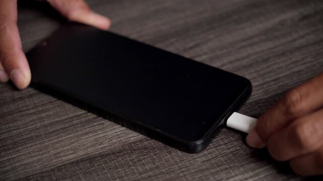 Close Up of USB C Cable Being Plugged into a Black Smartphone Lying on a Dark Wooden Desk