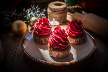 Delicious chocolate cupcakes topped with red buttercream, served on a ceramic plate with a warm festive atmosphere. Perfect sweet dessert for Christmas and New Year celebration.