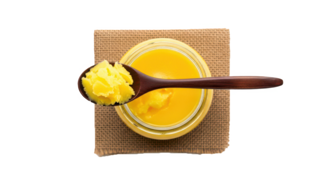 Wooden spoon with fresh yellow ghee in glass jar on rustic mat top view