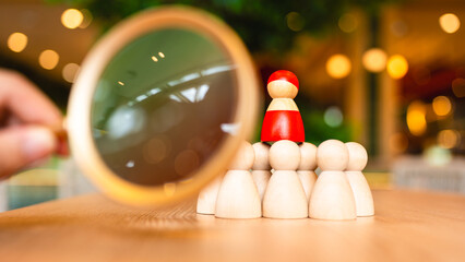 Close-up magnifying glass focusing on a red wooden figure among others, symbolizing leadership evaluation, talent selection, and human resource strategy in modern business environments.