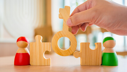 Wooden key piece connecting puzzle blocks between two toy figures in red and green, symbolizing...