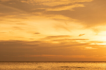 Fototapeta premium Nature sky breathtaking golden sunset over a calm ocean, with the entire sky and water bathed in brilliant shades of yellow and orange. Streaky clouds enhance the dramatic display of light 