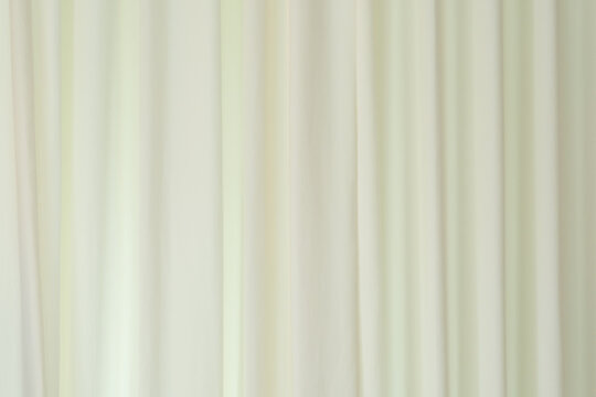Background of a creamy white or light beige fabric curtain. The curtain hangs in gentle, vertical folds, creating a smooth, flowing texture. The lighting is diffused, giving the fabric a subtle