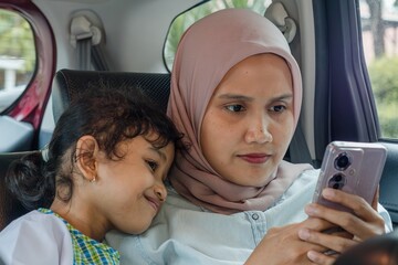 A muslim mother and her daughter enjoying a car trip while playing on smartphone.