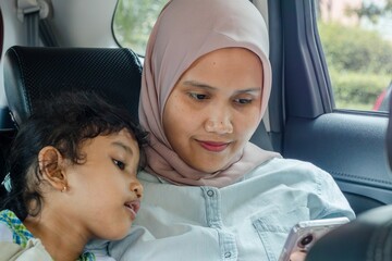 A muslim mother and her daughter using smartphone while traveling by car