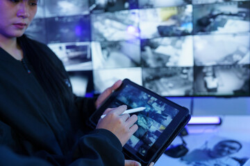 Focus on the iPad in the hand of the security guard checking the CCTV TV screen.