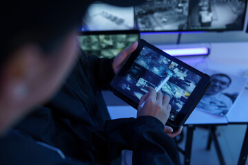 Focus on the iPad in the hand of the security guard checking the CCTV TV screen.
