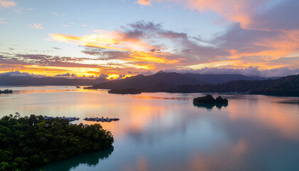 A breathtaking aerial view of a calm tropical lake dotted with small islands at sunrise. The vibrant orange and pink clouds beautifully reflect on the water surface.