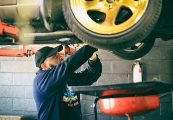 A mechanic sprays the underbody of a car raised on a lift.