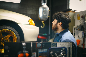 A mechanic sprays the underbody of a car raised on a lift.