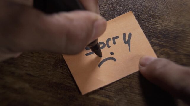 Hand writing sorry note with sad face emoticon