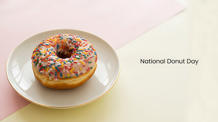 A colorful sprinkle-covered donut on a white plate against a pastel background, celebrating National Donut Day
