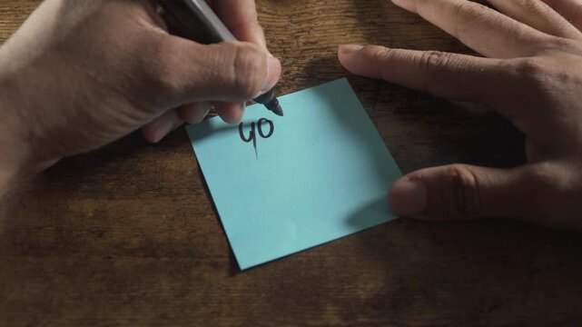 Person writing positive affirmation you are enough on a sticky note