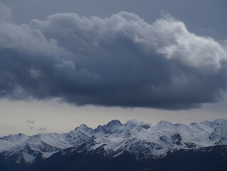 Snowy mountain range under a dramatic sky with heavy clouds creating a moody scene