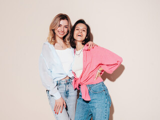 Two young beautiful smiling female in trendy summer clothes. Carefree women posing in studio....