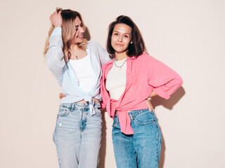Two young beautiful smiling female in trendy summer clothes. Carefree women posing in studio....