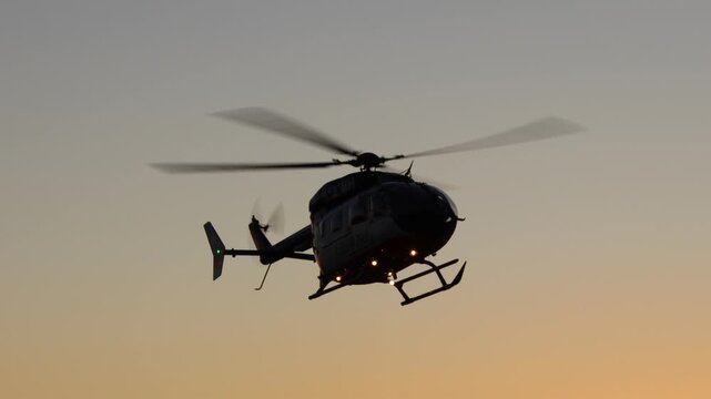 4K handheld video of a helicopter's rotor blades spinning in a silhouette outline with an orange gradient sunset sky behind it.