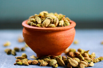 Dry cardamom seeds in clay pot on blue background.