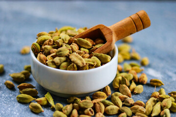 Heap of green cardamom seeds in bowl with wooden spoon on blue background