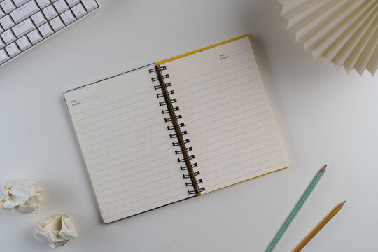 Open notebook with lined pages and two pencils on a minimalist white desk, ideal for office, study, or creative flat lay concepts.