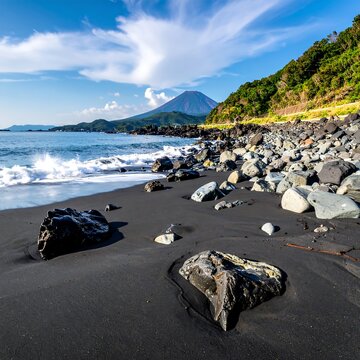 Coastal scene featuring black sand beach, rolling waves, and a distant peak