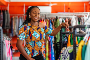 African woman, successful small business owner in ankara print dress stands proudly in her clothing...