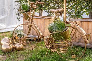 Ein zauberhaftes, ganz in Gold getauchtes Fahrrad steht als strahlendes Symbol der ewigen Liebe auf sattgrünem Rasen. Jeder Korb ist ein kleines Nest aus frischem Grün, zarten weißen Blüten und liebev