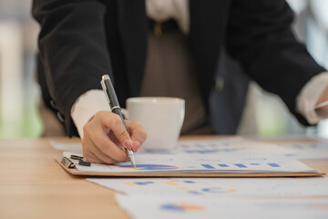 Close-up of a businesswoman's hand meticulously reviewing financial charts and graphs, using a pen...