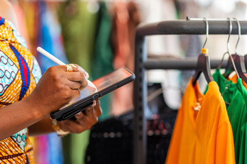 African woman, successful small business boutique owner, fashion entrepreneur checking inventory and managing online orders in her clothing store with her smart tablet, SME