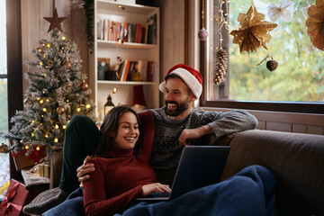Happy couple surfing the net on laptop while relaxing at home on Christmas.