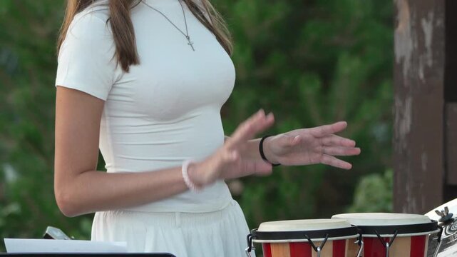 Percussion, woman, playing: Young woman playing bongo drums outdoors in a musical performance